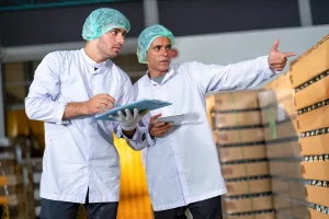Auditor y trabajador revisando procesos de inocuidad durante una implementación de ISO 22000 para MYPES en una planta de envasados.